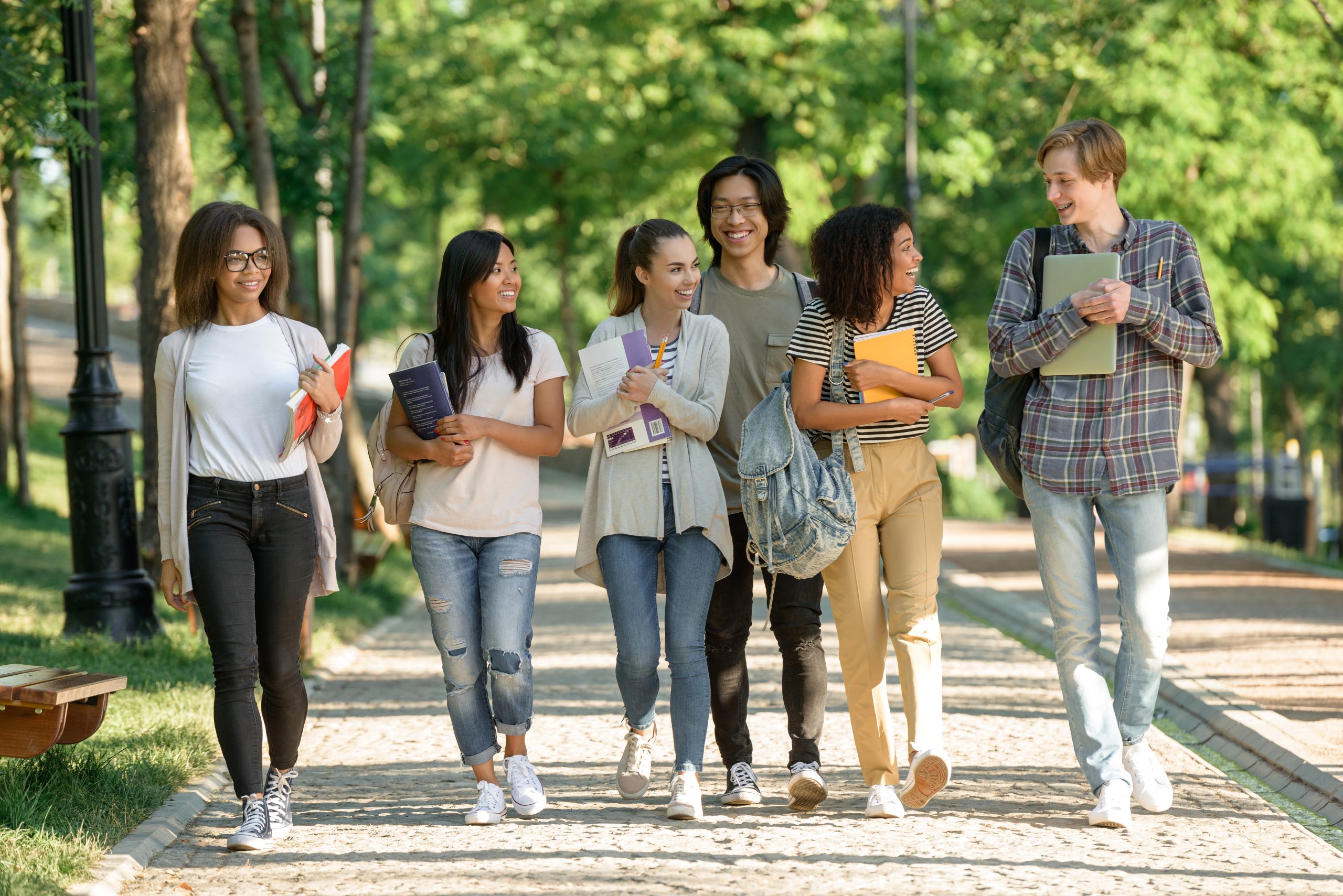 Picture of multiethnic group of young cheerful students walking while talking. Looking aside.